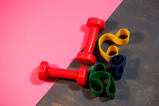 Red dumbbells and elastic bands for sports on a pink background. Healthy lifestyle. Fitness equipment for weight training. Muscle development and fitness training