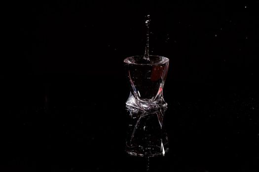 Black background is a glass in which a drop of water falls. Splashing water on glass