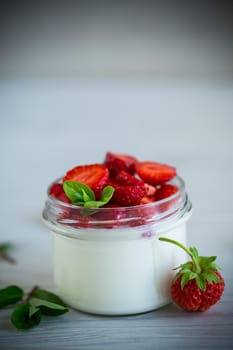 Sweet homemade yogurt with fresh ripe strawberries in a glass jar on a light wooden table