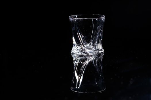 Black background stands a clean glass with reflection on a glass table. Facets on a Glass Cup