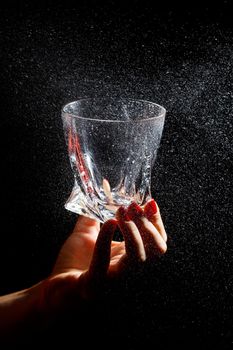 Black background on it is a close-up of a clean glass in a hand. Spray on a glass of water. Insulated glass