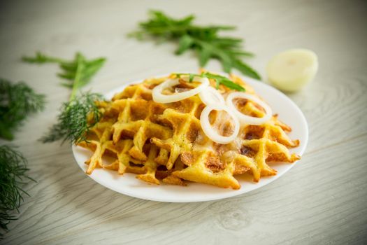 fried potato cheese vegetable waffles with bacon and onions in a plate, on a wooden table.