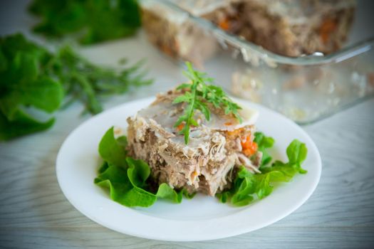 jellied meat with greens and vegetables in a plate on a wooden table