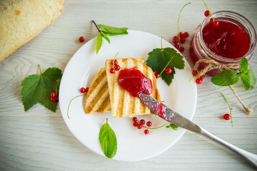 fried bread croutons for breakfast with redcurrant jam in a plate with berries on a wooden table.