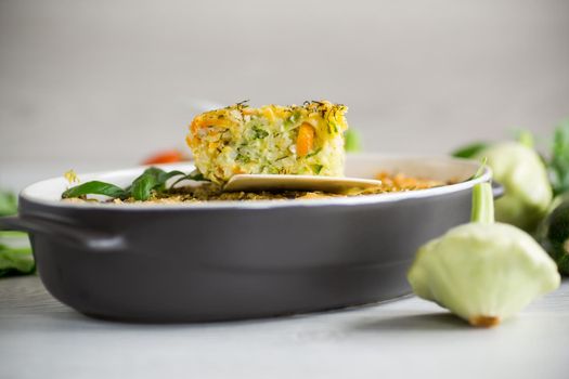 vegetable casserole of patissons, zucchini, carrots in a ceramic form on a light wooden table.