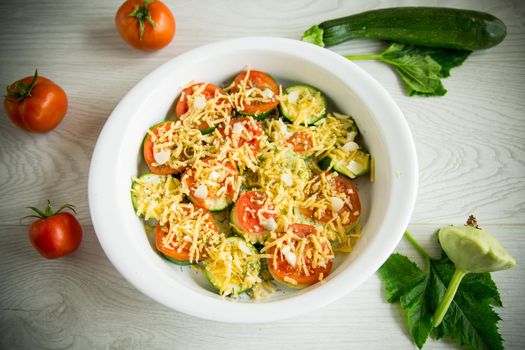 raw zucchini and tomatoes sliced with cheese, prepared for baking in a ceramic dish.