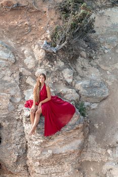 A girl with loose hair in a red dress sits on a rock rock above the sea. In the background, the sea. The concept of travel