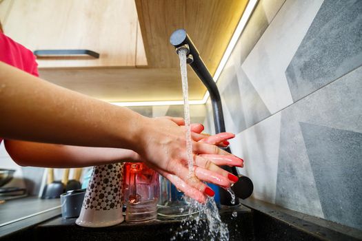 The girl washes her hands under running water in a black washstand. Water faucet, clean dishes, wooden kitchen furniture