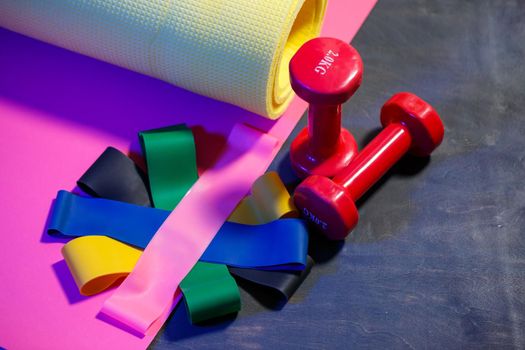 Red dumbbells, fitness mat and elastic bands for sports on a pink background. Healthy lifestyle. Fitness equipment for weight training. Muscle development and fitness training