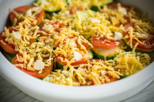 raw zucchini and tomatoes sliced with cheese, prepared for baking in a ceramic dish.