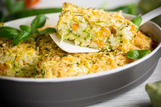 vegetable casserole of patissons, zucchini, carrots in a ceramic form on a light wooden table.