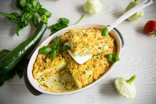 vegetable casserole of patissons, zucchini, carrots in a ceramic form on a light wooden table.