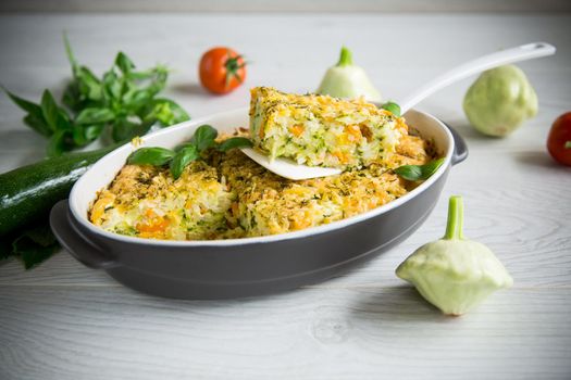vegetable casserole of patissons, zucchini, carrots in a ceramic form on a light wooden table.