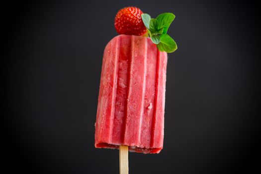 cooked homemade strawberry ice cream on a stick, isolated on black background