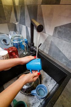 Hands with sponge wash the cup under water, housewife woman in washing blue mug in a kitchen sink with a blue sponge, Hand cleaning, manually, housework dishwasher