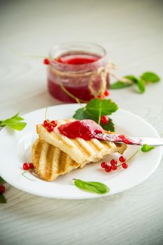 fried bread croutons for breakfast with redcurrant jam in a plate with berries on a wooden table.