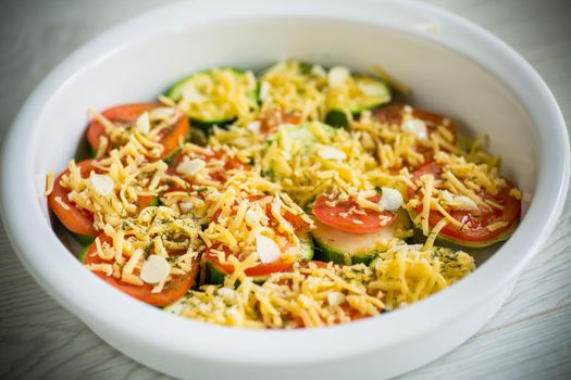 raw zucchini and tomatoes sliced with cheese, prepared for baking in a ceramic dish.