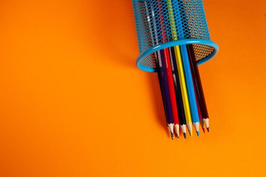 blue metal bucket with colored pencils for office on an orange background