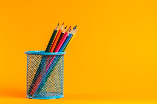 blue metal bucket with colored pencils for office on an orange background