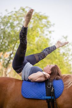 young woman doing yoga on a horse against the backdrop of trees.