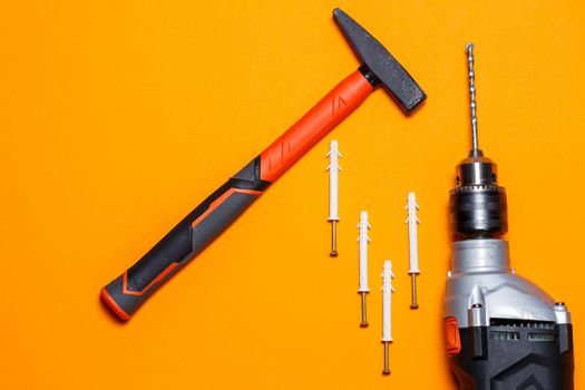Tools for repair. Hammer for nails, drill, dowel in the wall on an orange background. Toolkit for the wizard
