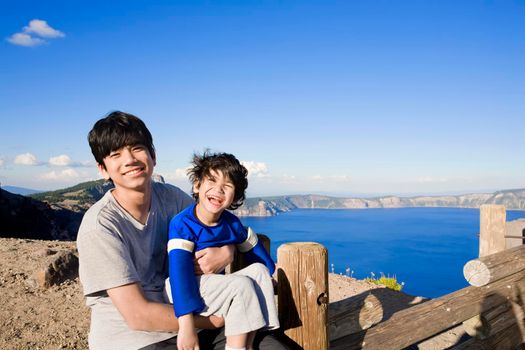 Teen brother holding young special needs sibling outdoors by Crater Lake
