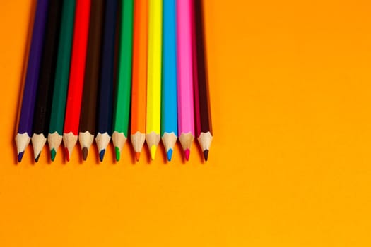 multicolored pencils for drawing stacked on an orange background. Stationery items