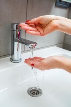 White sink with a silver faucet in the bathroom. Gray can with liquid soap for hands. Turning on the tap water, personal hand hygiene. Hand washing under running water
