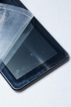 Black scratched tablet with a protective film on a gray background. Protect your device screen