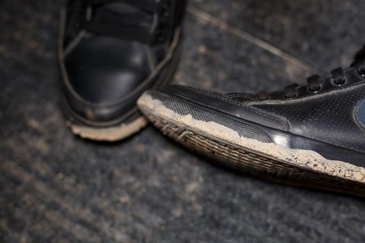 dirty shoes standing on a black carpet with a scattered swamp