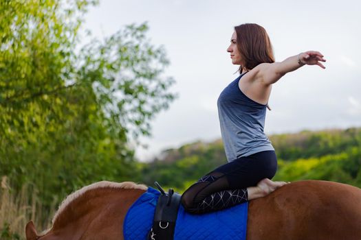 young woman doing yoga on a horse against the backdrop of trees.