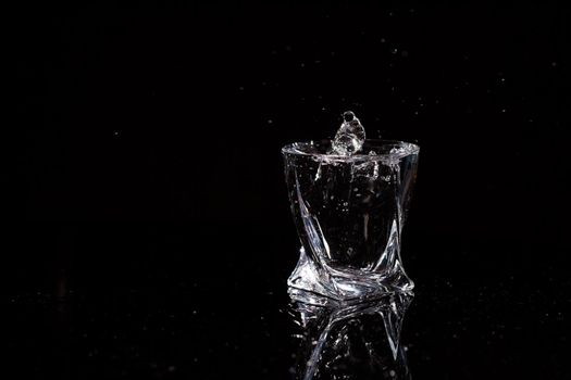 Black background is a glass in which a drop of water falls. Splashing water on glass