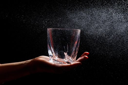 Black background on it is a close-up of a clean glass in a hand. Spray on a glass of water. Insulated glass