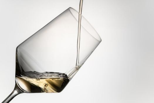 close-up of pouring white wine into a crystal glass. filling white wine into a crystal glass isolated on a grey background. image to cut out. beverage concept. Hard ligth