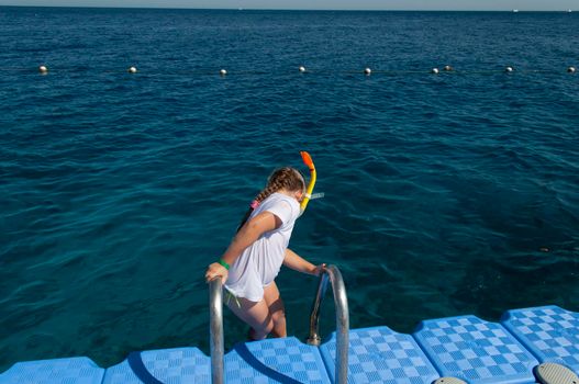 a little girl in a white t-shirt and a swimming mask, dives and swims in the salty Red Sea in Egypt, refreshes on a hot day, summer vacation adventure, summer vacation adventure. High quality photo