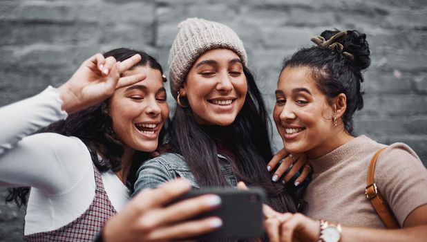 We never run out of moments to take selfies. Cropped portrait of an attractive group of sisters standing together and taking a selfie with a cellphone in the city