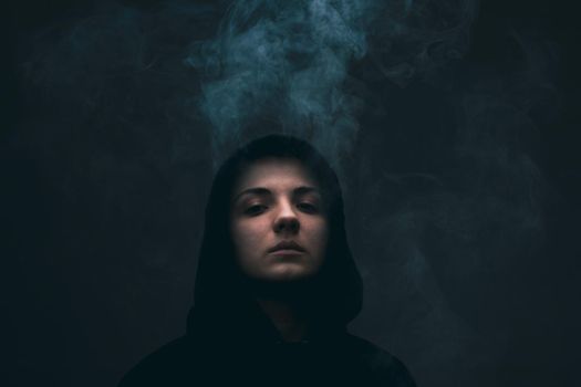 Dark portrait of a short haired girl wearing hoodie with smoke coming out of it.