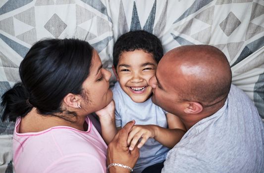 You guys are embarrassing me. a cheerful young couple kissing their son on the cheek while hanging out on the bed at home during the day