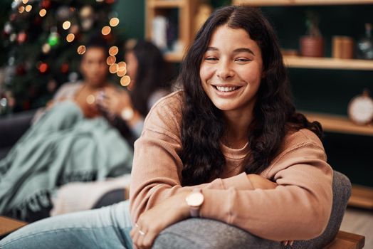 All I want for Christmas, Ive already got. a beautiful young woman relaxing on the sofa with her friends in the background during Christmas at home