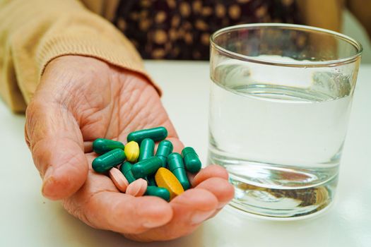 Asian elderly woman holding pill drug with water in glass, strong healthy medical concept.