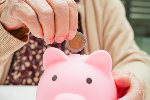 Retired elderly woman putting coins money in piggy bank and worry about monthly expenses and treatment fee payment.