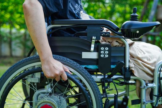Asian elderly woman disability patient sitting on electric wheelchair in park, medical concept.