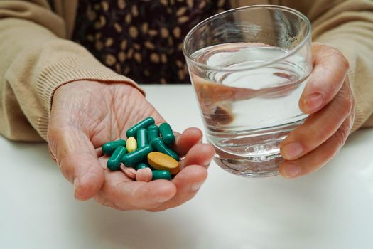 Asian elderly woman holding pill drug with water in glass, strong healthy medical concept. 