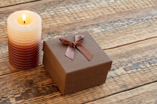 Brown gift or present box and burning candle on old wooden boards. Top view. Holiday concept.