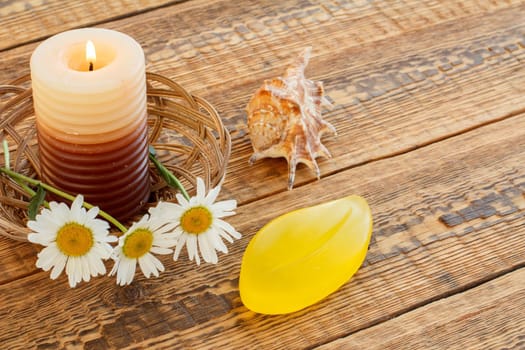 Bouquet of chamomiles, perfume, burning candle and white gift or present box on wooden boards. Top view. Holiday concept.