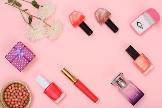 Gift boxes, powder, nail polish, bottles of perfume, lipstick, brush and flowers on a pink background. Women accessories. Top view.