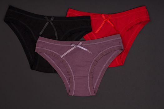 Beautiful black, brown and red cotton panties on the dark background. Woman underwear set. Top view.