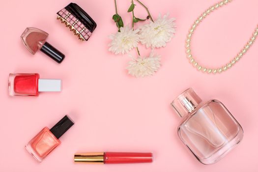 Lipstick, bottles with nail polish, hair clip, flowers, beads and bottle of perfume on a pink background. Women cosmetics and accessories. Top view.
