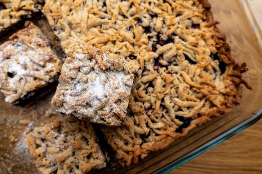 Sliced homemade grated berry pie, in a glass baking dish on a wooden board. Homemade cakes