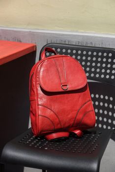 Red leather casual unisex backpack on a black chair. Outdoors photo